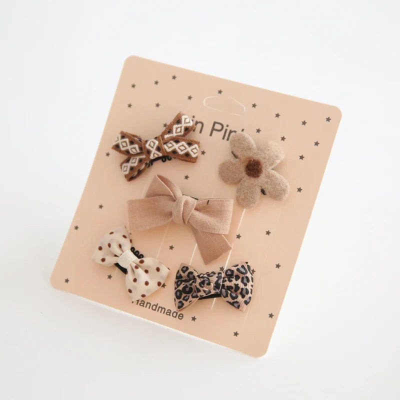 Set of five neutral-toned baby hair clips with bows and a flower, featuring varied patterns.