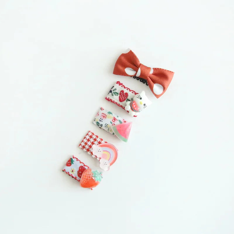 Set of five colorful baby hair clips with bows, fruit, and rainbow designs on a white background.