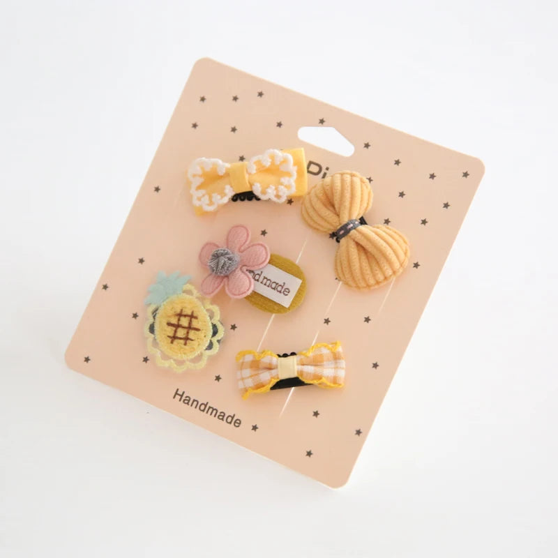 Set of five yellow and pink cotton baby hair clips with bows, flower, and pineapple designs on a peach card.