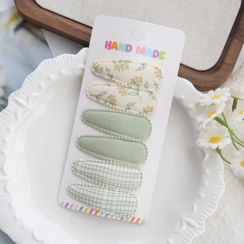 Handmade set of 6 fabric hair clips for babies and girls, featuring floral, solid sage, and gingham patterns.