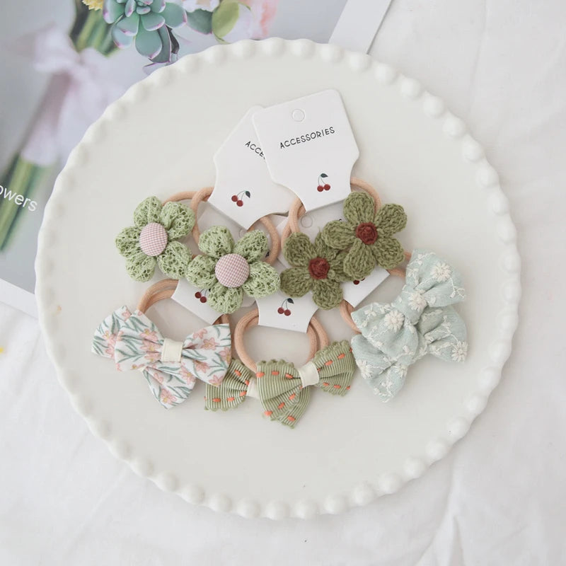 Handmade floral and bow hair ties for girls, featuring green crochet flowers and patterned fabric bows.