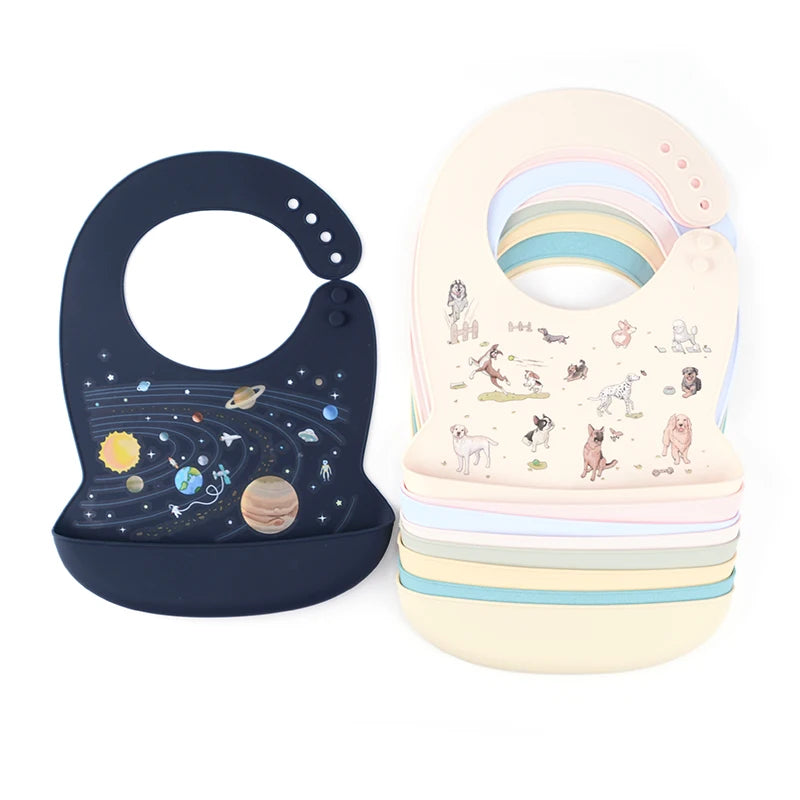 Two waterproof silicone baby bibs: one dark blue with a solar system design, and a stack of pastel bibs with animal patterns.