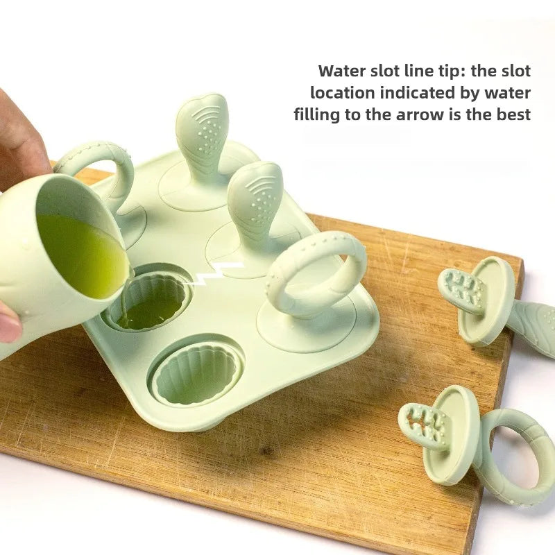 Green silicone baby popsicle mold with 4 cells, being filled with green liquid, on a wooden board.