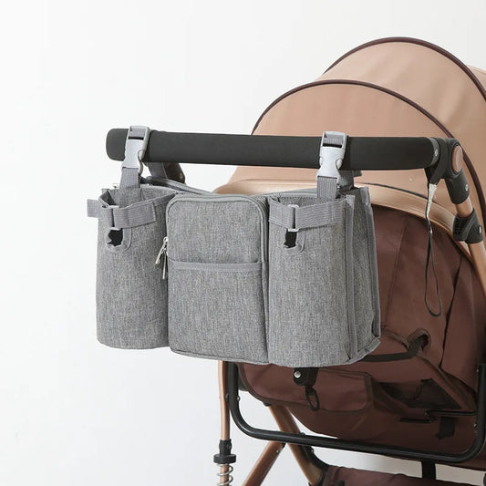 Gray waterproof stroller organizer bag with multiple compartments and cup holders, attached to a brown stroller.