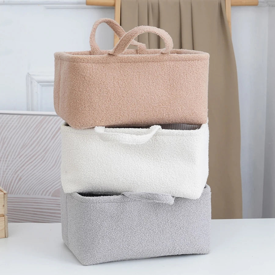 Stack of three soft polyester baby organizers in beige, white, and gray with handles.