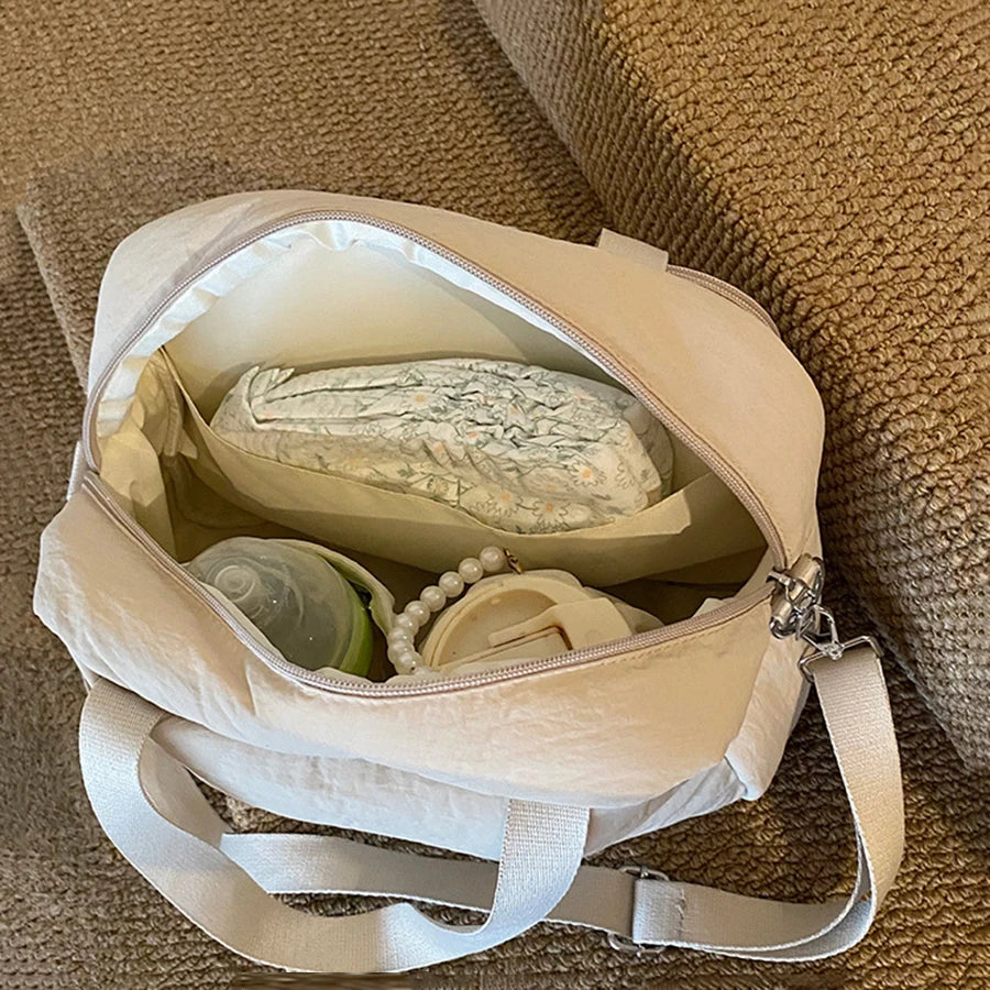 Beige polyester diaper bag, open with diapers, bottle, and accessories inside.