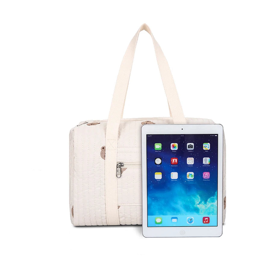 Beige quilted diaper bag with top handles, front zipper pocket, and dimensions shown next to a tablet.