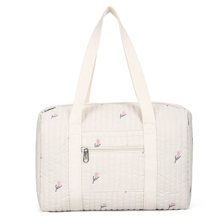 Quilted cream diaper bag with pink floral embroidery, front zipper pocket, and sturdy top handles.