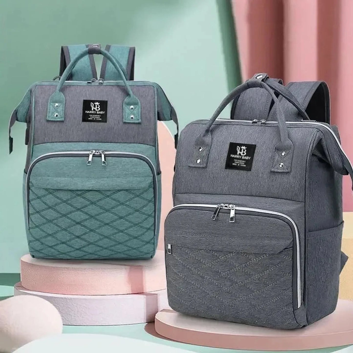 Two large Oxford fabric diaper backpacks, one gray and teal, the other dark gray, with quilted pockets.