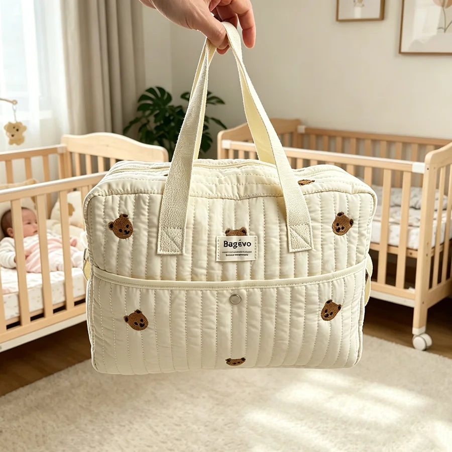Quilted cream diaper bag with brown bear embroidery, large capacity, held in a nursery.