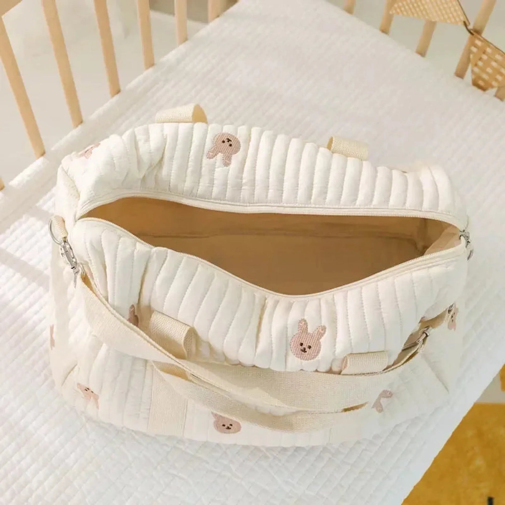 Quilted cream cotton diaper bag with cute bunny embroidery and open top, resting in a crib.