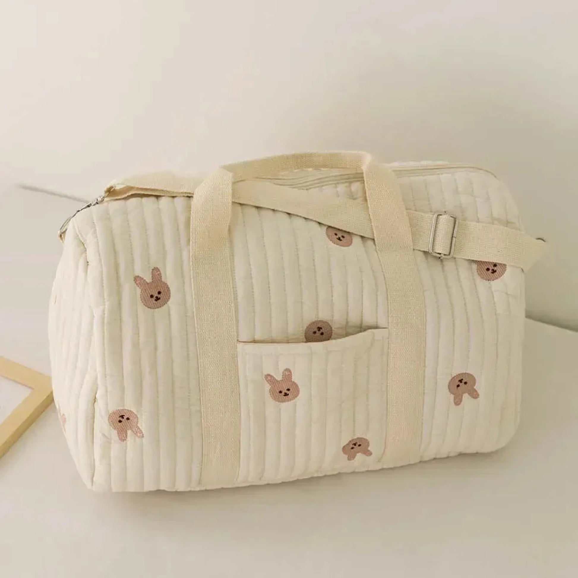 Quilted cream cotton diaper bag with brown bunny embroidery, front pocket, and shoulder strap.