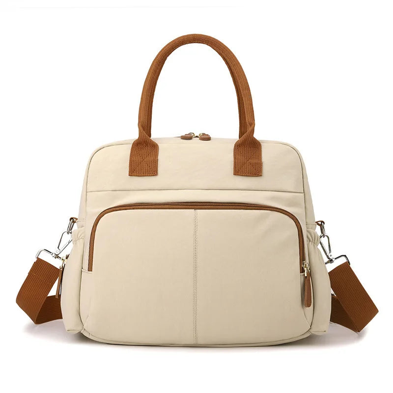 Beige diaper bag with brown handles and shoulder strap, featuring front pockets and a modern design.