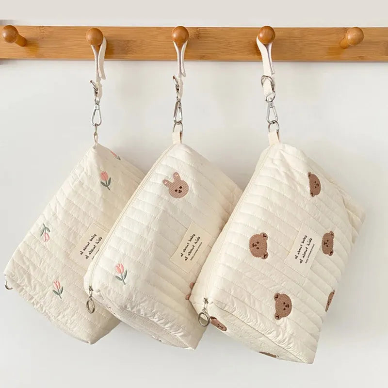 Quilted cream cotton baby changing bags with embroidered designs: flowers, bunny, and bears.