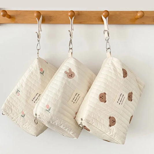 Quilted cream cotton baby changing bags with embroidered designs: flowers, bunny, and bears.